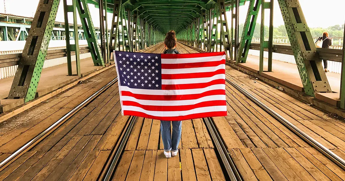 Jeune femme de dos sous un pont à Manhattan tenant un drapeau des États-Unis.