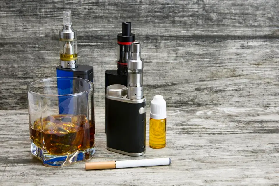 Cigarettes électroniques, verre d'alcool et cigarette sur une table.