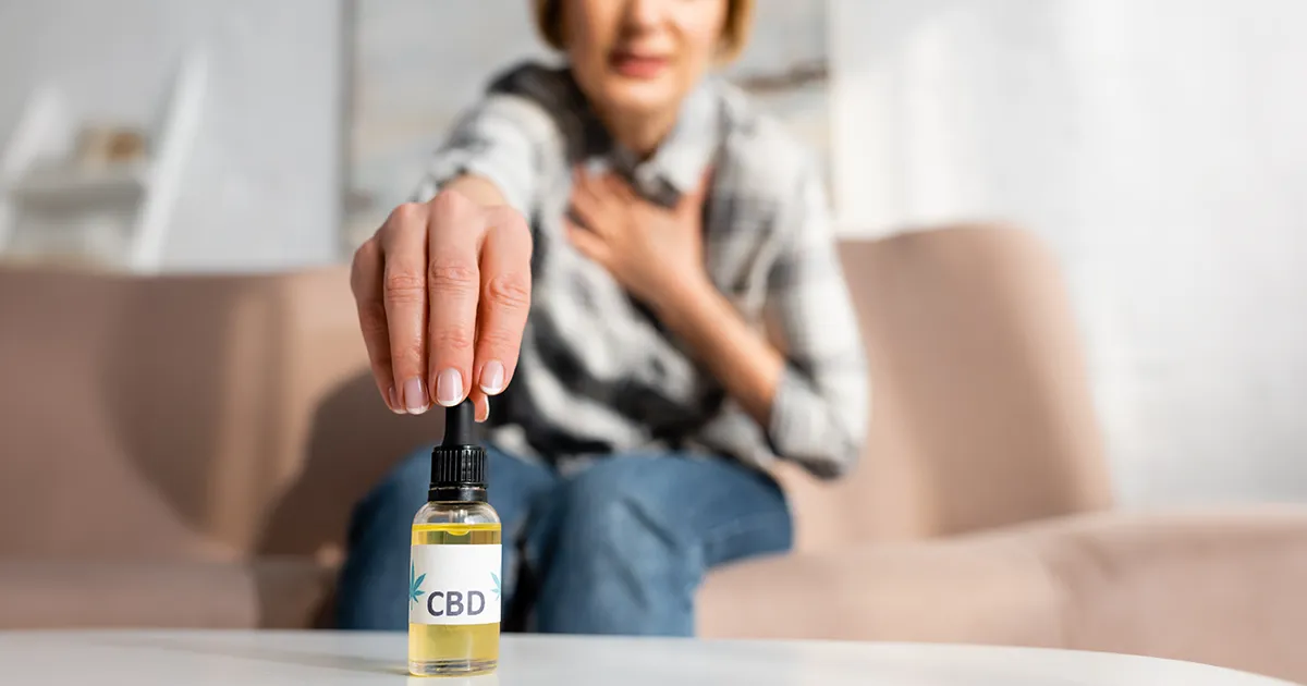 Grand mère consommant une huile de CBD assise sur son canapé.