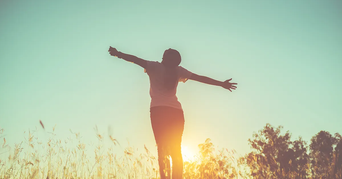 Femme debout les bras en croix face au soleil car elle est en pleine santé